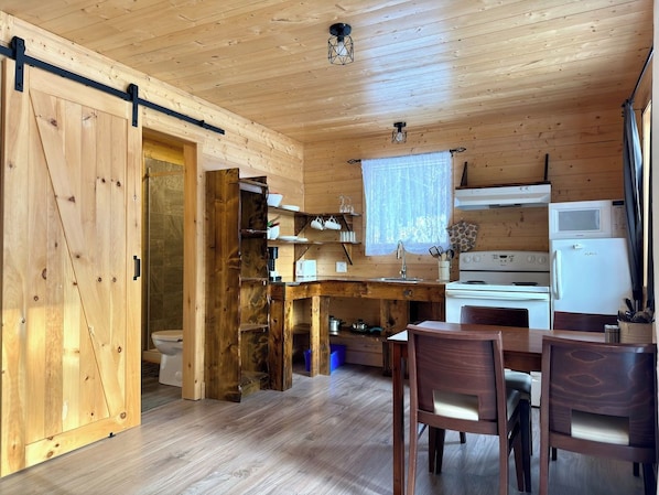 Interior de madera con cocina, que incluye estufa, refrigerador y mesa de comedor con sillas.