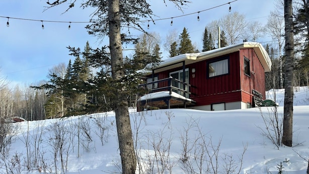 A red cabin with a balcony, surrounded by snow and trees.