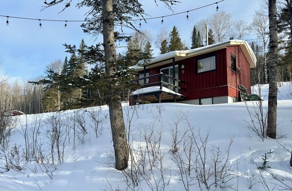 A red cabin with a balcony, surrounded by snow and trees.