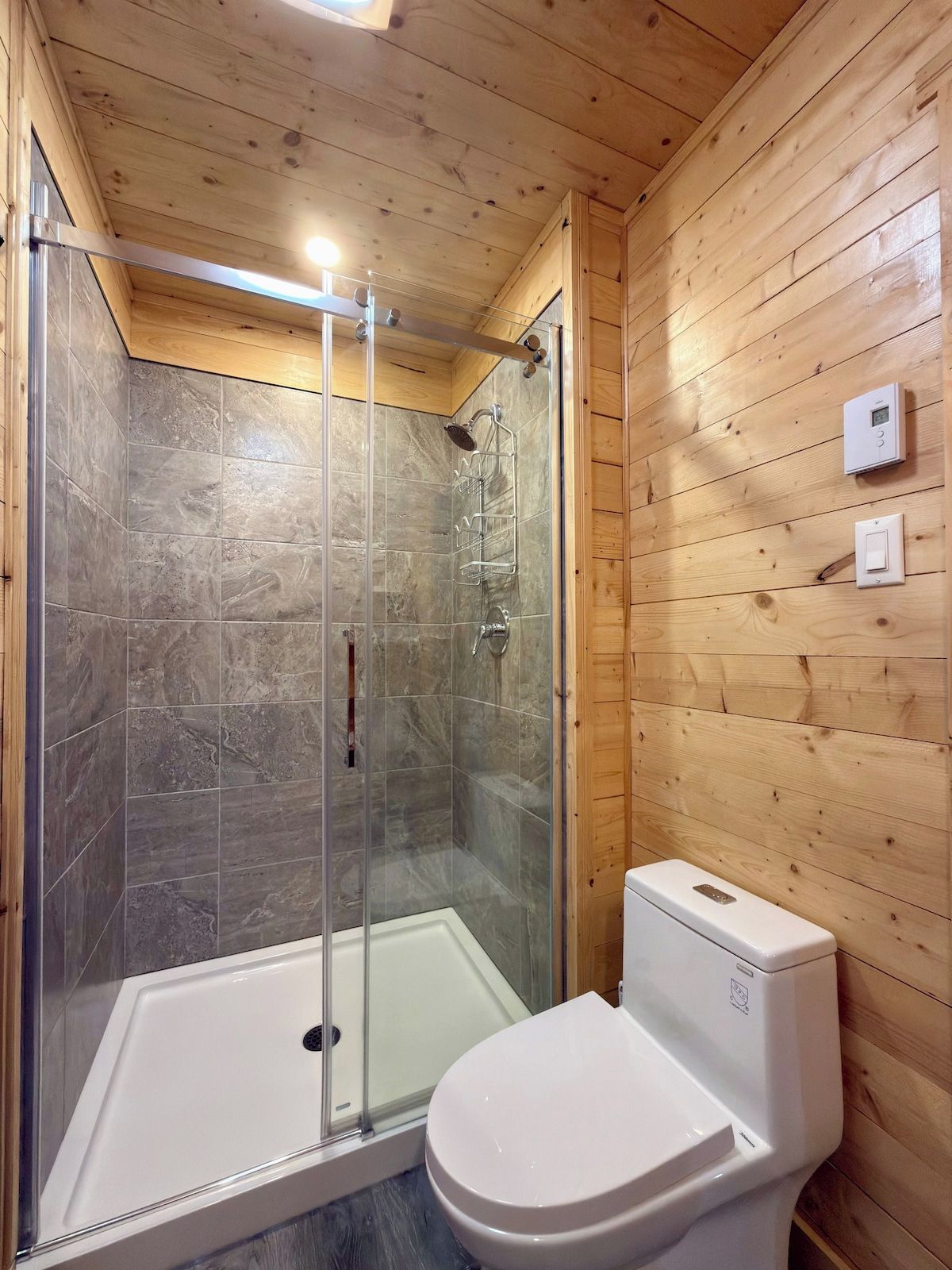 A bathroom with a shower enclosure, a toilet, and wooden paneling.