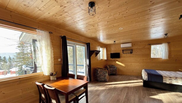 A wooden cabin interior with a dining table, chairs, a sofa, and a TV mounted on the wall.