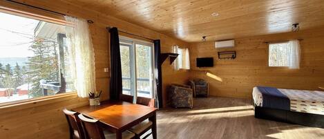 Interior de una cabaña de madera con una mesa de comedor, sillas, un sofá y un televisor montado en la pared.