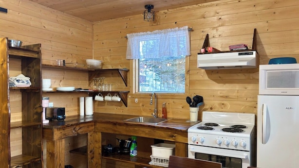 A wooden cabin kitchen with a stove, sink, and window. - A Peaceful Retreat Away from the Noise, Close to What Matters Most (Pohénégamook)