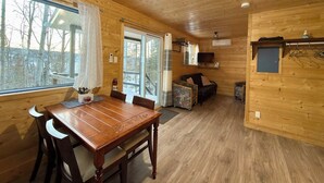 A wooden cabin interior with a dining table, chairs, a sofa, and a television. - A Peaceful Retreat Away from the Noise, Close to What Matters Most (Pohénégamook)