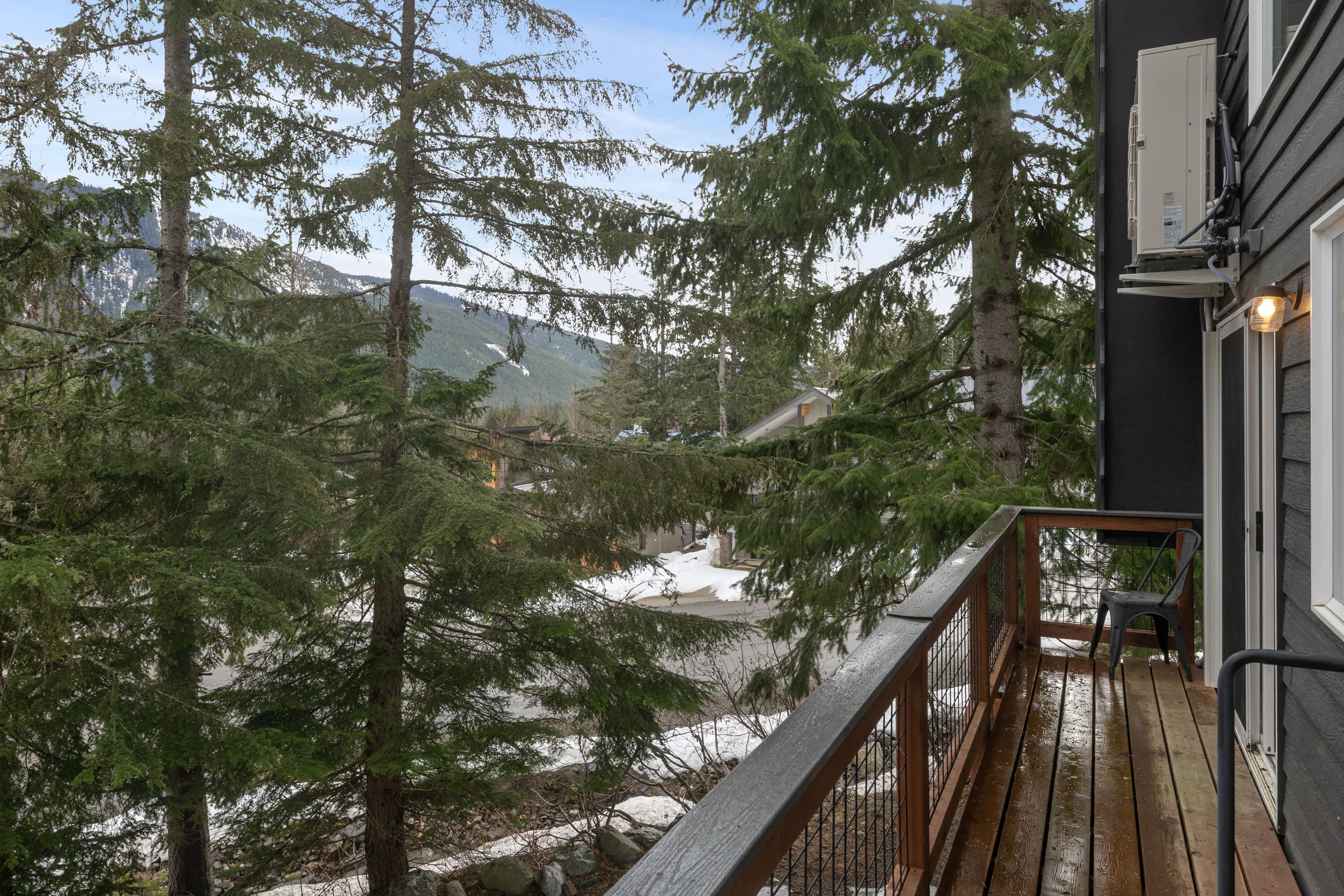 Eine Holzdar Terrasse mit Metallgeländer, das auf eine verschneite Landschaft und hohe Nadelbäume blickt.