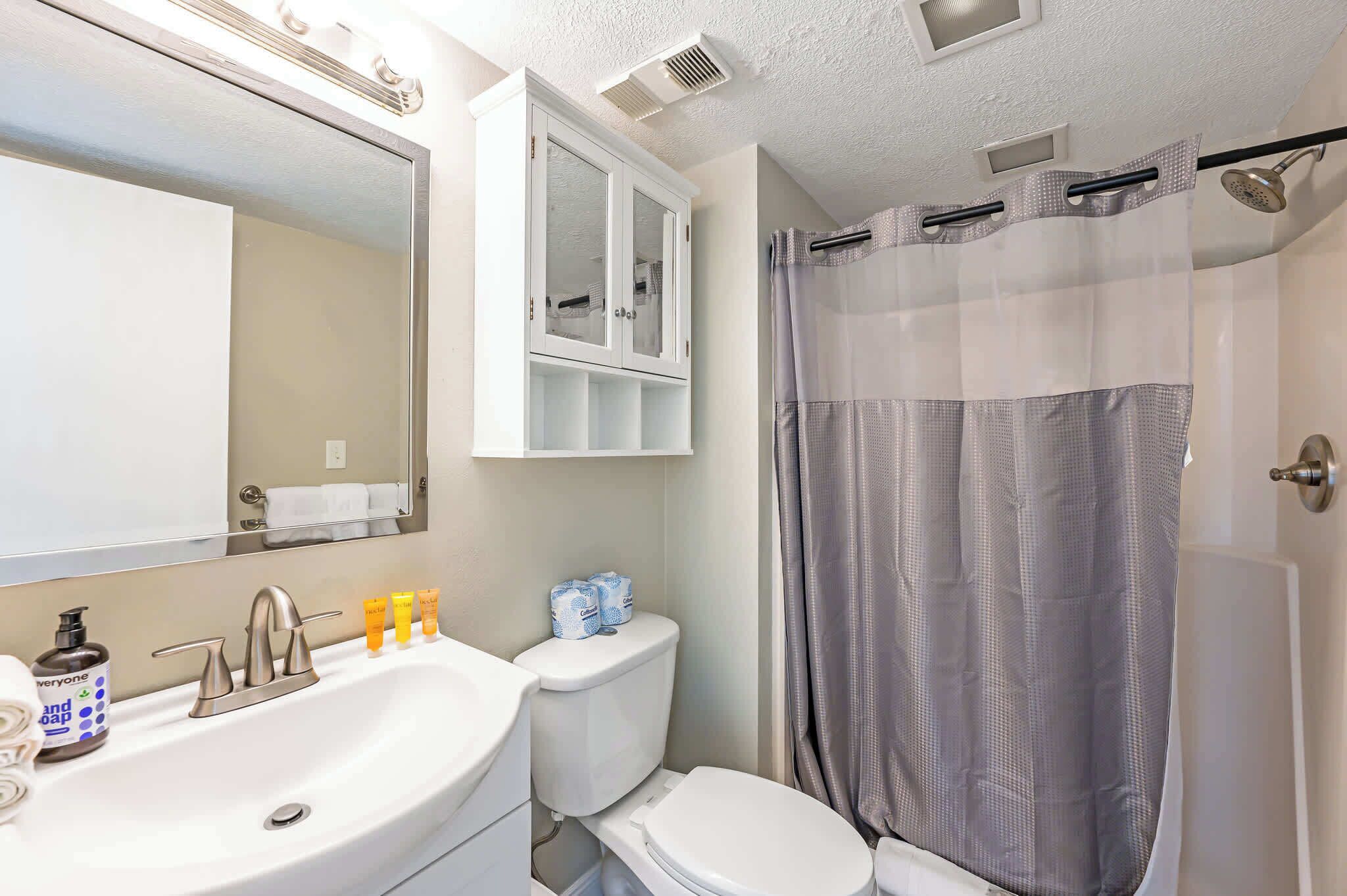 Un baño con lavamanos blanco, espejo, armario, inodoro y cortina de ducha.