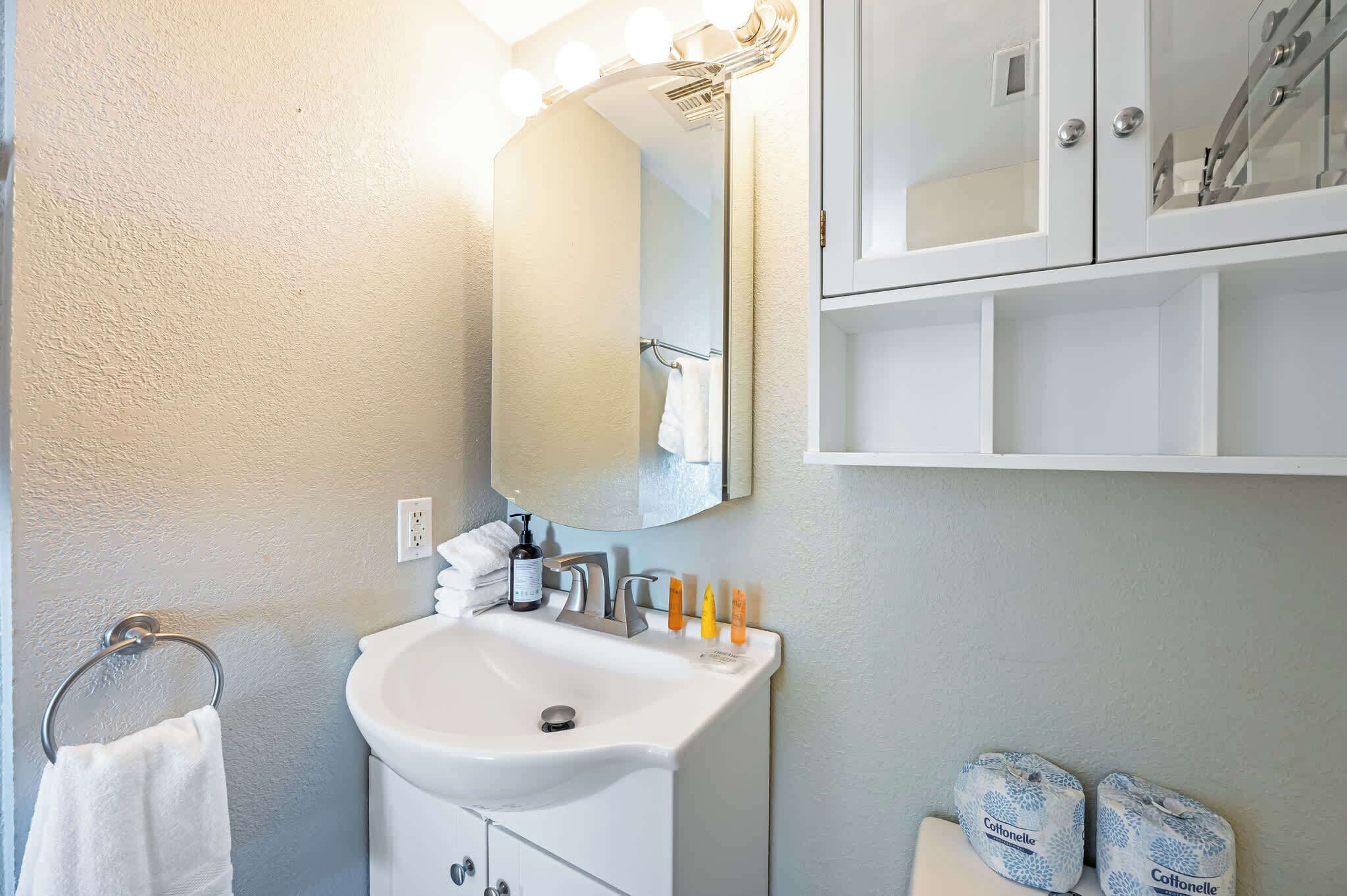 Une salle de bain avec un lavabo blanc, un miroir et un meuble-vasque. On y trouve des articles de toilette sur le lavabo et un porte-serviettes avec une serviette blanche.