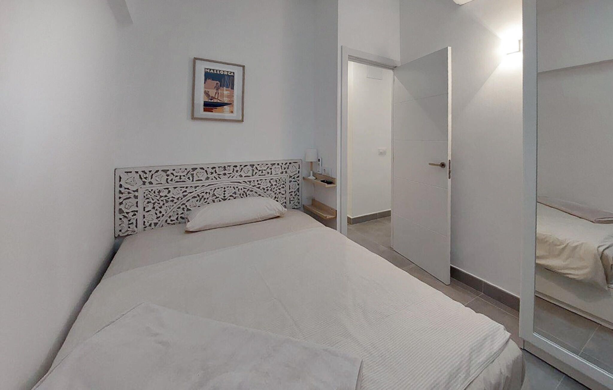 A bedroom with a bed, a nightstand, a framed picture on the wall, and a door leading to another room.