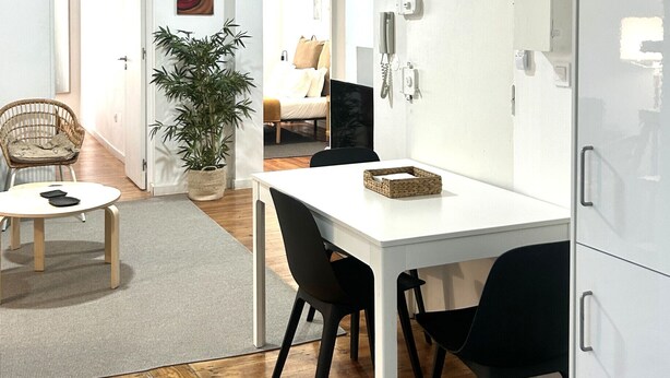 Een modern interieur met een eettafel, stoelen, een hanglamp, een potplant en een wit kastje.