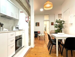 A modern kitchen with white cabinets, a built-in oven, and a dining area with a table and chairs. - SJ2E Spacious & Comfortable | DT | A/C (Lisboa ciudad)