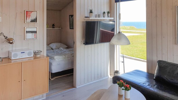A cozy room with a bed, a TV, a wooden cabinet, a small table with flowers, and a view of the sea. - Pet friendly home in Sydals with WiFi (Sydals)