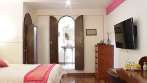 A bedroom with a bed, a dresser, a television, and an open door leading to a bathroom.