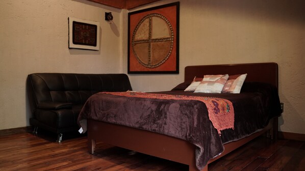 A bedroom with a bed, a chair, a wall clock, and a framed artwork. - Hotel Coyoacan (Mexico City)