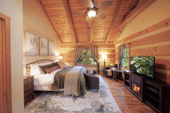 A bedroom with a bed, a television, a fireplace, and a ceiling fan.