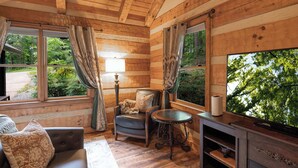 Interior de una cabaña de troncos con sofá, sillón, mesa y televisor.