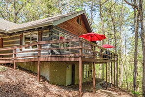 A cabin with a wooden deck, a covered outdoor seating area, and a forested backdrop.
