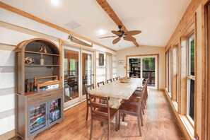 A dining area with a long wooden table, chairs, a ceiling fan, and a wooden cabinet with shelves.