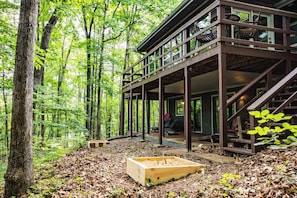 A wooden cabin with a deck, surrounded by a forest.
