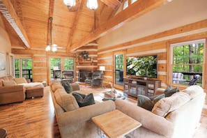 A log cabin interior with a living room, fireplace, and large windows.