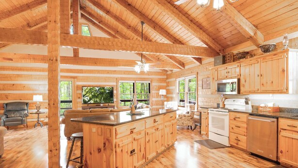 Una cabaña de troncos espaciosa con una cocina grande, pisos de madera y un comedor con vistas al exterior.