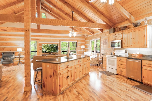 A spacious log cabin with a large kitchen, wooden floors, and a dining area with a view of the outdoors.