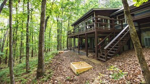 Una cabaña de madera con un balcón y escaleras, rodeada de un bosque.