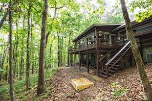 A wooden cabin with a deck and stairs, surrounded by a forest.