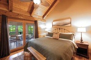 A wooden-paneled bedroom with a bed, bench, and a view of an outdoor patio.