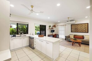 Una cocina moderna con armarios blancos, una isla central y un comedor con sofá y mesa de centro.