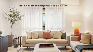 A living room with a beige sofa, a coffee table, a lamp, and a potted plant. - Family Entertainer in Kanimbla - Space & Privacy (Kanimbla)