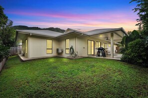 Una casa moderna de dos pisos con un porche cubierto, un patio pequeño y vistas de las colinas circundantes.