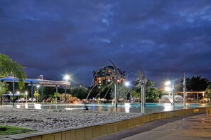 A nighttime view of a beach area with a pool, a large metal sculpture, and a building in the background. - Family Entertainer in Kanimbla - Space & Privacy (Kanimbla)