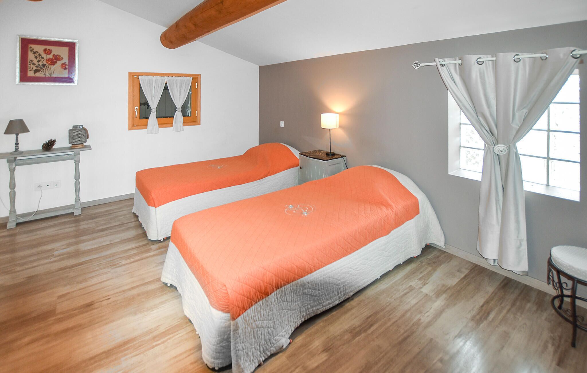 Une chambre avec deux lits, une petite table avec une lampe, un tableau au mur et une fenêtre avec des rideaux.