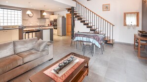 A spacious living area with a sofa, coffee table, dining table with chairs, a kitchen area, and a staircase. - Maison avec piscine 1 (Mormoiron)