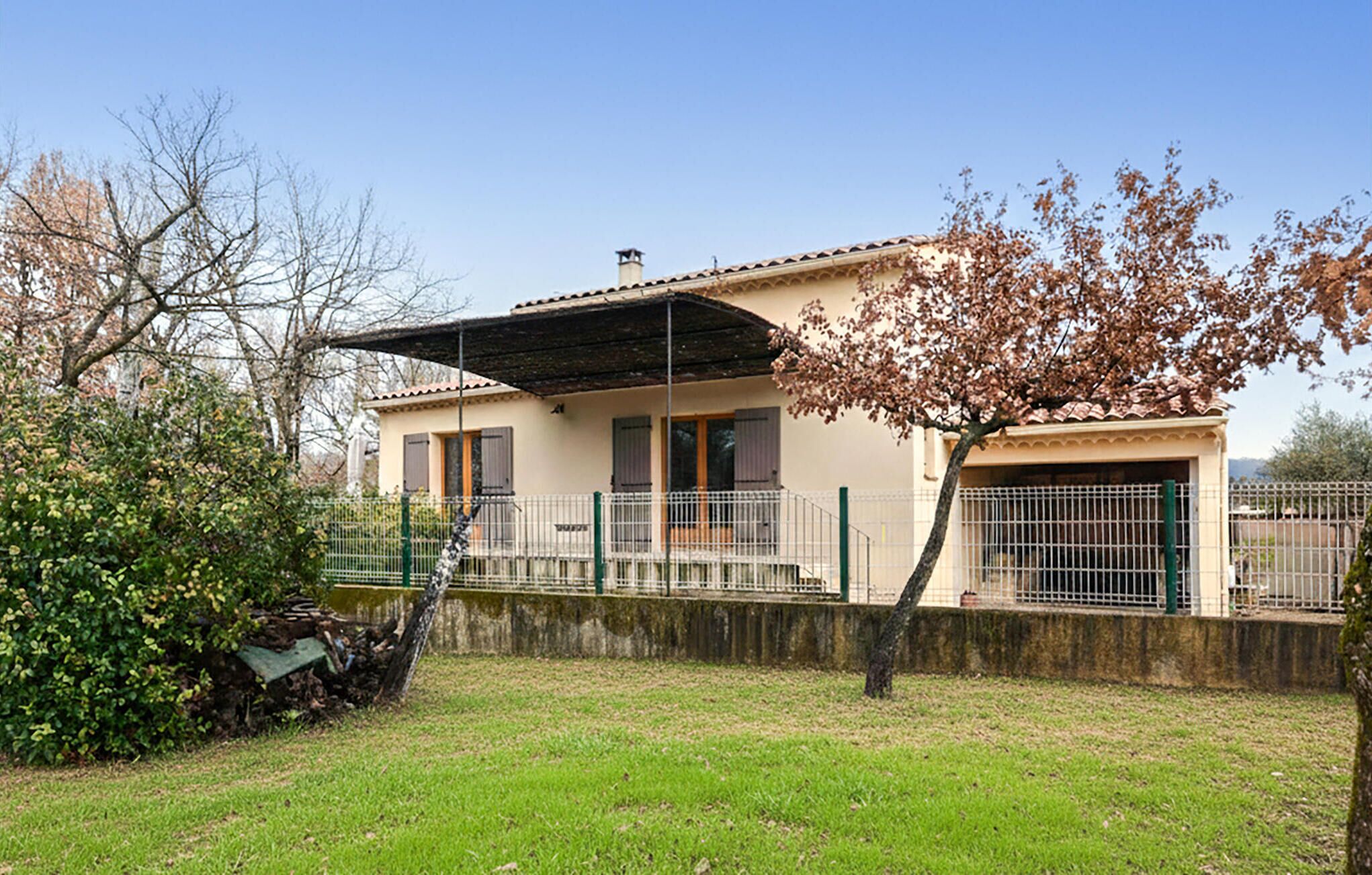 Una casa de dos pisos con un porche cubierto, un patio cercado y un árbol con flores rosadas.