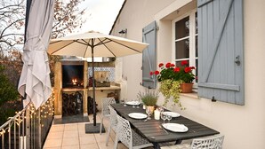 An outdoor dining area with a table set for two, a fire pit, and a potted plant with red flowers. - Maison avec piscine 1 (Mormoiron)