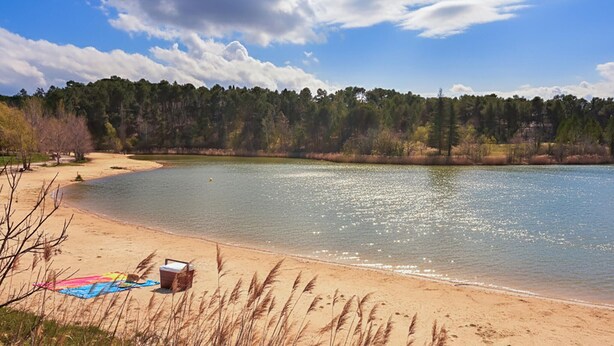 A beach with a sandy shore, a small boat, and a picnic setup. - Maison avec piscine 1 (Mormoiron)