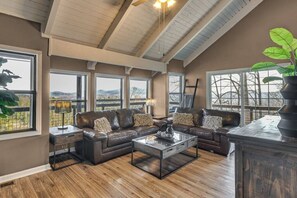 A spacious living room with a large sectional sofa, a glass coffee table, and a view of the outdoors through large windows. - Mountain Views, Peaceful Waterfall 3 King Bedrooms (Pickens)