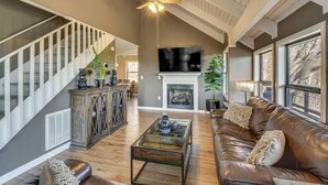 A spacious living room with a fireplace, a large TV, and a staircase. - Mountain Views, Peaceful Waterfall 3 King Bedrooms (Pickens)