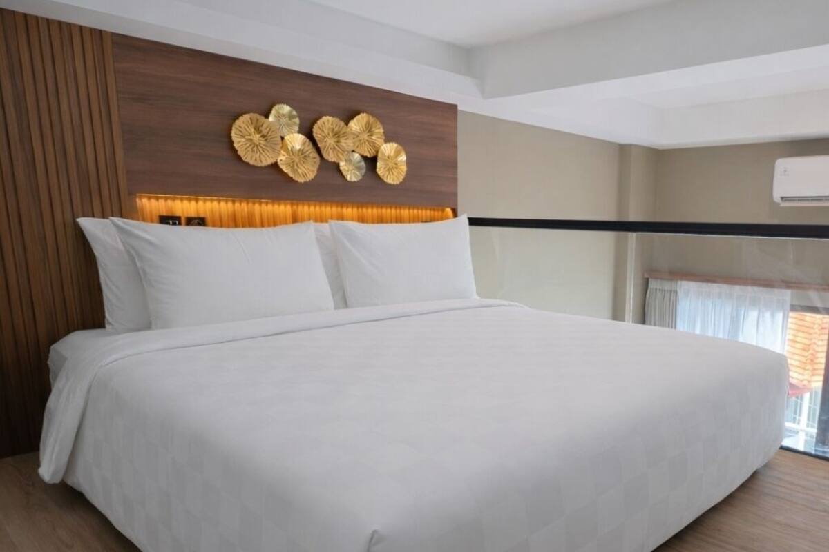 Moderni hotellihuone, jossa on suuri sänky, puupanelointi ja koristeellinen seinäelementti.