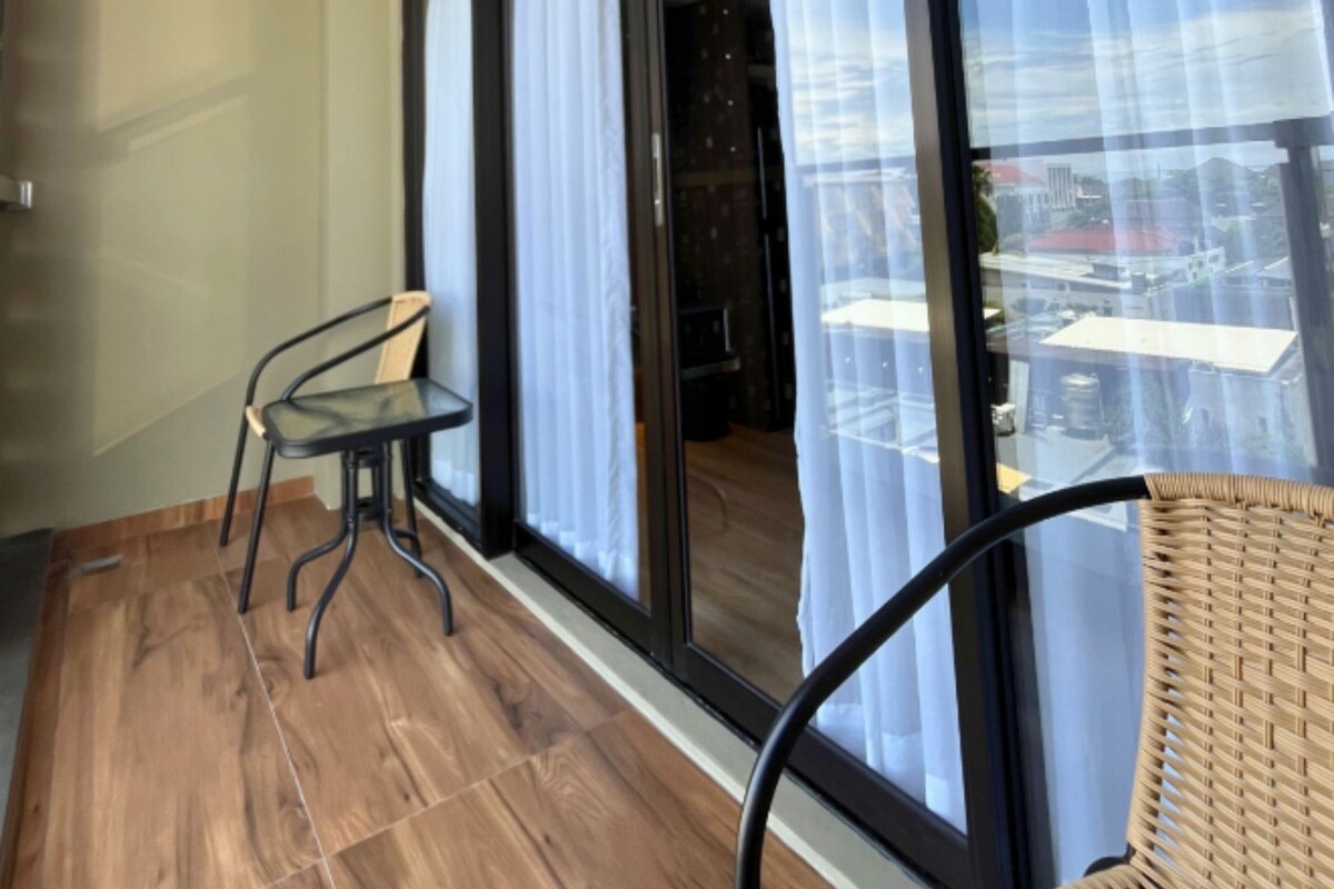 A balcony with a wooden floor, two chairs, and large windows with curtains.