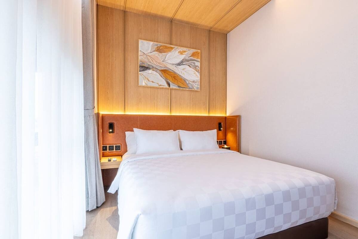 Hotellihuone, jossa on sänky, puinen pääty, yöpöydät ja taulu seinällä.