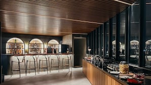 A modern bar area with a wooden ceiling, bar stools, and a counter with various food items and bottles. - JJ JIVANA BALI (Tibubeneng)