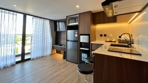 A modern kitchen with a built-in oven, a coffee machine, and a sink. There is a bar area with stools and a large window with curtains. - JJ JIVANA BALI (Tibubeneng)