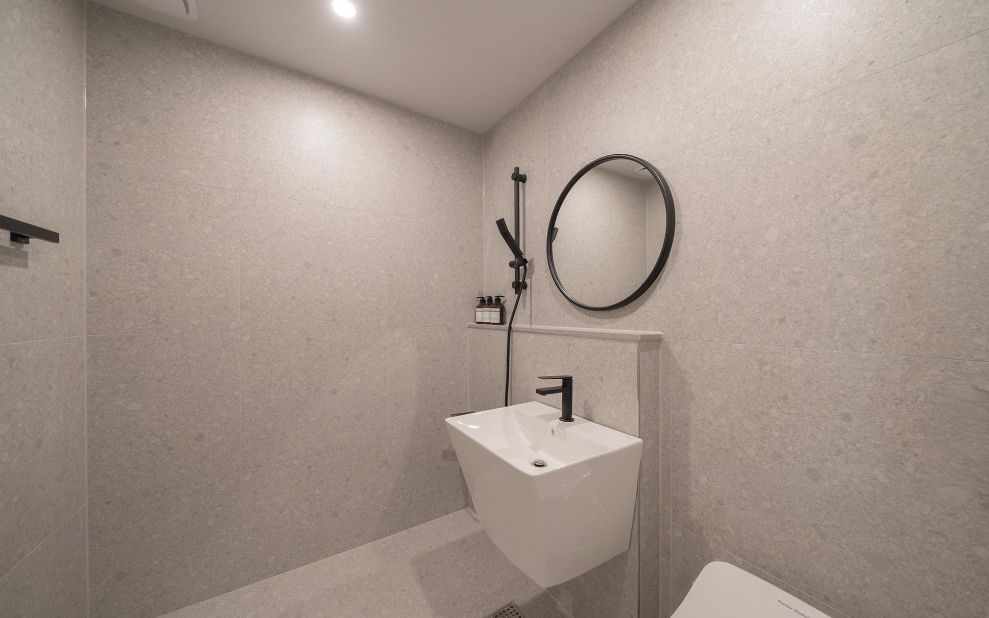 Un baño moderno con un lavabo blanco, un cabezal de ducha de mano y un espejo redondo.