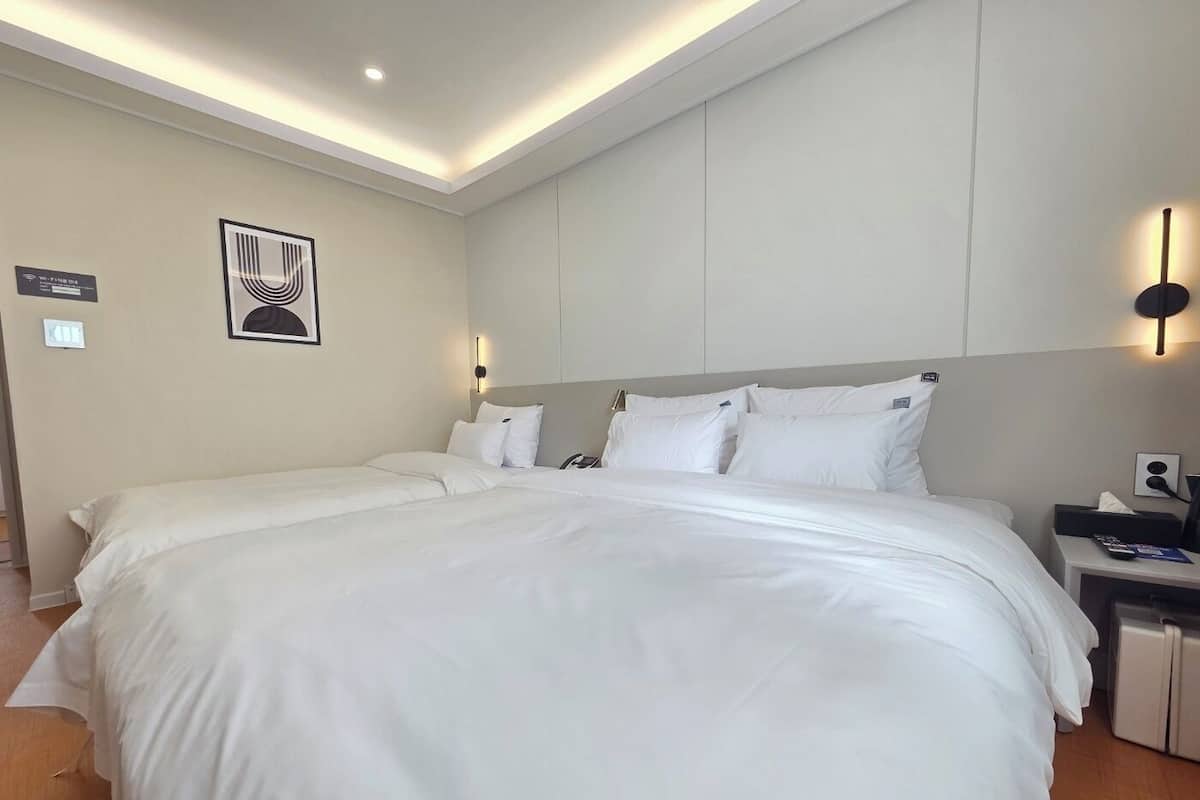 Una habitación de hotel con una cama grande, una mesita de noche, una lámpara de pared y un cuadro enmarcado.