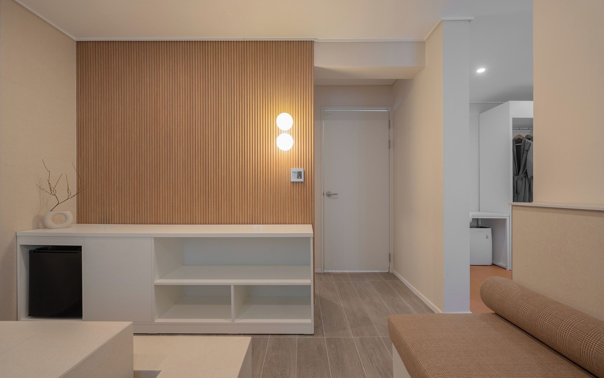 A modern interior with a wooden panel wall, a white console table, a seating area with a patterned cushion, and a clothing rack.