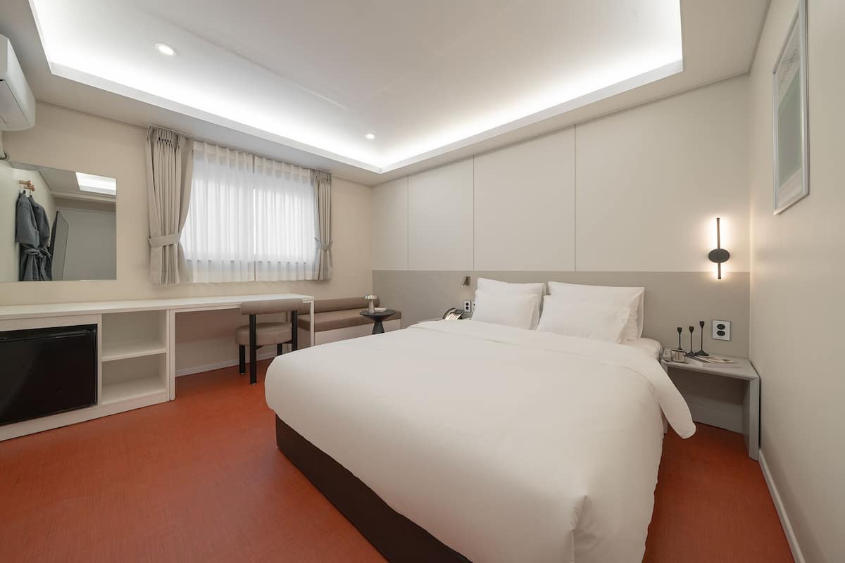 Una habitación de hotel moderna con una cama grande, un escritorio, una silla, un televisor y una ventana con cortinas.