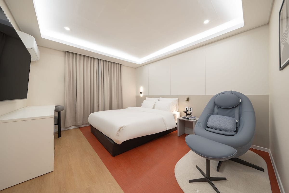 Una habitación de hotel moderna con cama, escritorio, silla y mesita de noche.