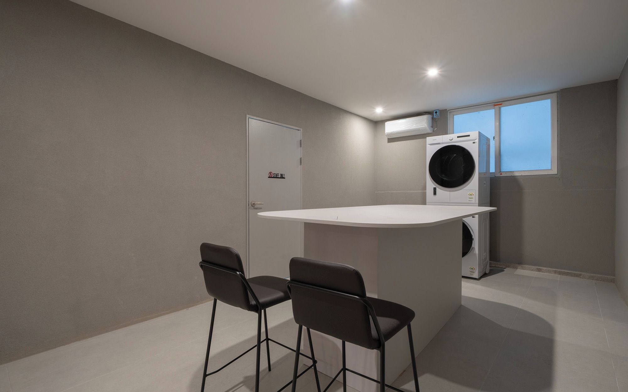 A compact kitchen with a built-in washing machine, a small bar area with stools, and a door marked 'Staff Only'.